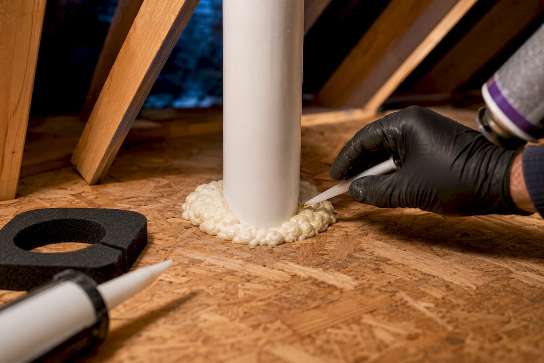 Technician sealing attic plumbing penetration