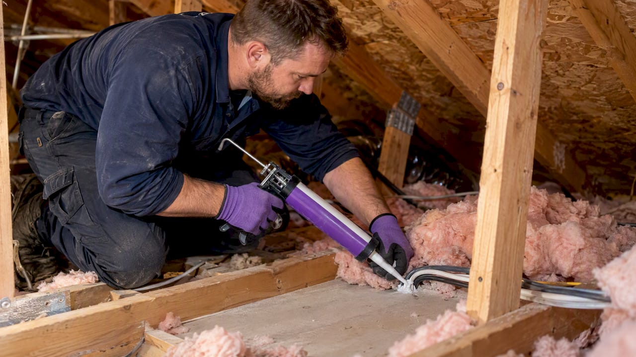 Technician sealing a ceiling gap beneath attic insulation