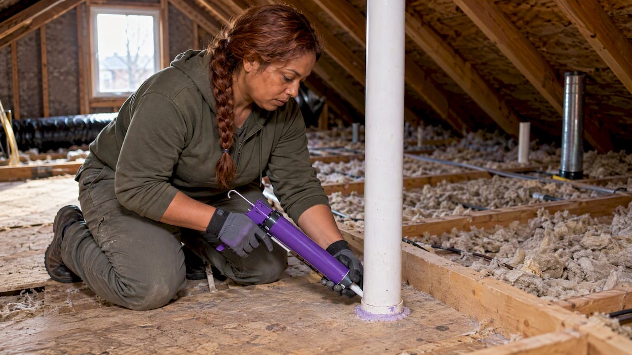 Technician sealing an attic floor pipe penetration